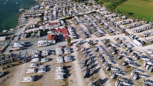 A cinematic horizontal drone high angle shot showcasing hundreds of sailboats and luxury yachts organized in dry dock rows for winter storage at Ionian Marine shipyard in Aktio Preveza, Greece.
