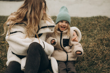 Happy young mother hugging her cute laughing little daughter while sitting on a grass lawn in a park on an autumn day. © Irina