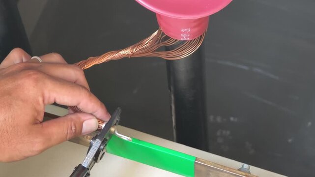 Close up video of electrician hand using a tool to crimp a metal terminal lug onto copper shield ground wire for switchgear earth connection.