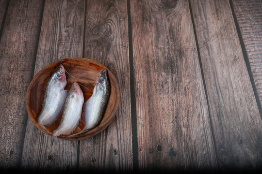 Close-up of fresh raw Ompok bimaculatus (Pabda/Parda fish) arranged in a wooden bowl on a natural wooden background. Ideal for Bengali cuisine, seafood, aquaculture, healthy nutrition, and fresh.