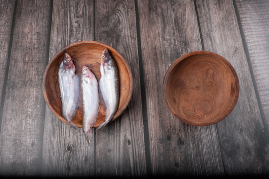 Close-up of fresh raw Ompok bimaculatus (Pabda/Parda fish) arranged in a wooden bowl on a natural wooden background. Ideal for Bengali cuisine, seafood, aquaculture, healthy nutrition, and fresh.