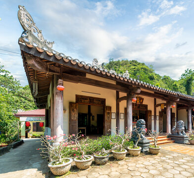 Traditional Vietnamese temple architecture at the Abbot's Quarters, Marble Mountains, Da Nang, Vietnam, featuring ornate roof details, stone guardian lion statues and flowering desert rose plants