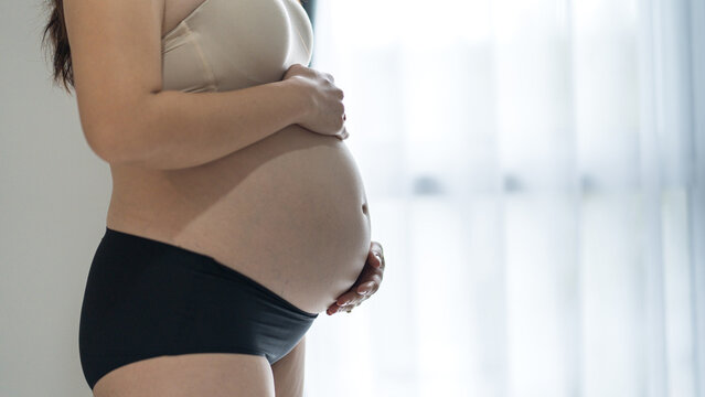 Pregnant woman holding her baby bump, highlighting maternal care and healthy pregnancy.