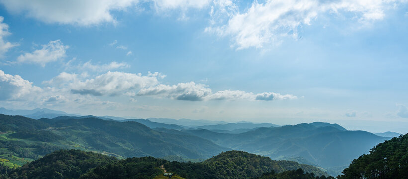 Panoramic mountain landscape with blue sky, clouds, and layered forested hills