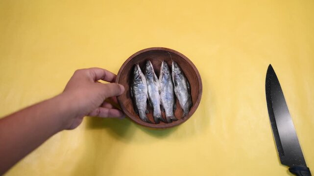 Close-up 4K video of a fresh raw Ompok bimaculatus (Pabda/Parda fish) in a wooden bowl held by an Indian man against a yellow background. Seafood, aquaculture, nutrition, and fresh market concepts.