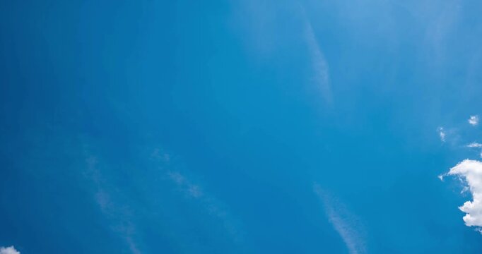 Straight up view time lapse of white cumulus clouds moving across a blue sky with an airplane vapor contrail