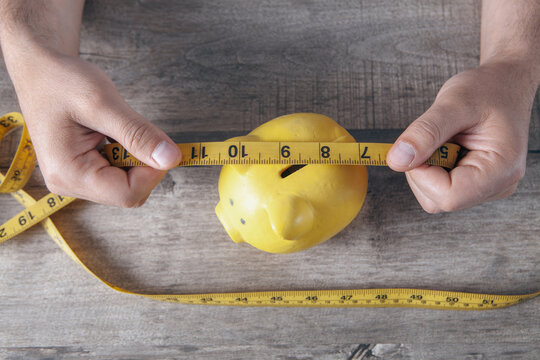 Man's hands holding a  piggy bank with a measuring tape on a wooden background