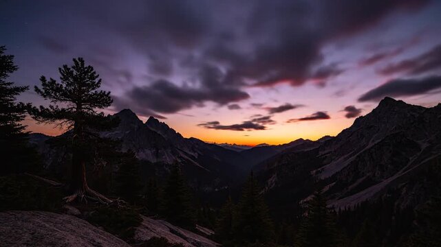Sunset over a mountain range with trees on a rocky outcrop at dusk