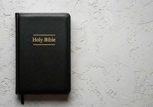 Black Leather Holy Bible with Gold Lettering on a Textured Gray Concrete Background with Copy Space