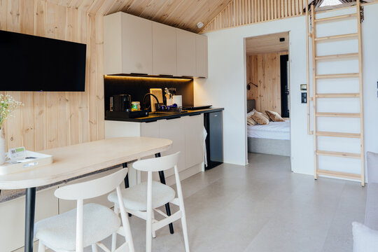 Warm modern tiny house interior with wooden ceiling, kitchenette, dining area and cozy bedroom