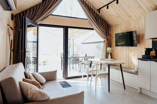 Bright modern tiny house living room with wooden walls, sofa, dining table and terrace