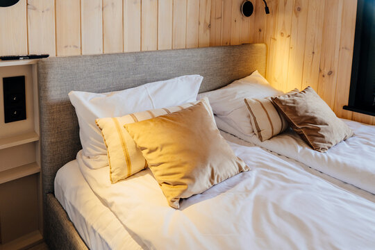 Cozy wooden cabin bedroom with soft pillows, warm light and grey upholstered bed