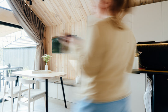 Blurred woman moving inside bright wooden tiny house kitchen and dining interior