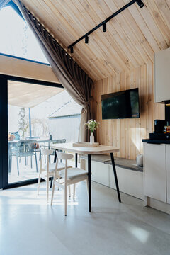 Vertical shot of sunny tiny house dining area with wooden walls, terrace and large window
