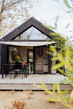 Vertical shot of modern eco cabin exterior with wooden terrace and glass facade
