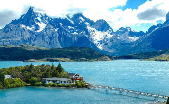 A small island with a red house surrounded by turquoise waters, with the dramatic peaks of Torres del Paine rising in the background, Patagonia, Chile
