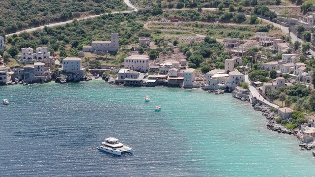 Aerial of Limeni village on turquoise waters on a sunny day, traditional stone built manioc tower houses on sea shore and mountains in backdrop