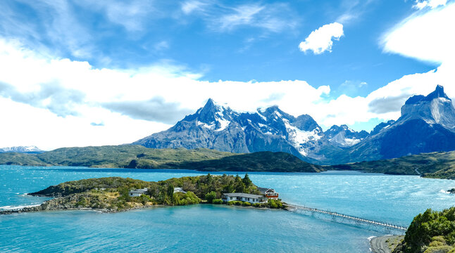A small island with a red house surrounded by turquoise waters, with the dramatic peaks of Torres del Paine rising in the background, Patagonia, Chile