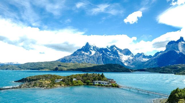 A small island with a red house surrounded by turquoise waters, with the dramatic peaks of Torres del Paine rising in the background, Patagonia, Chile