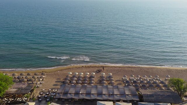 Drone of Kourouta Beach with sun umbrellas and calm Ionian Sea in Ilia Greece, aerial establishing pullback