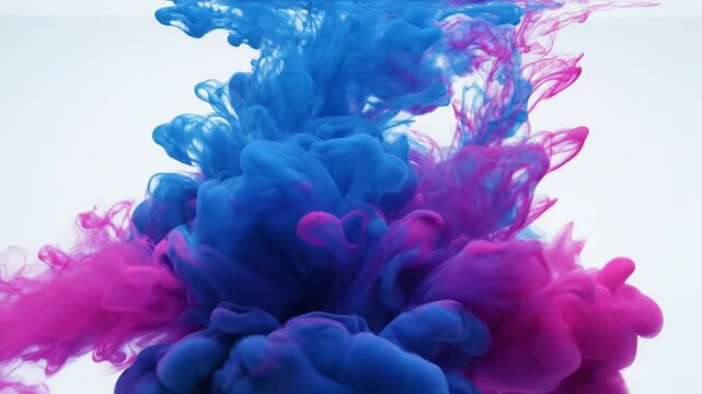 Vibrant blue and pink ink swirls mix in water creating a mesmerizing display of colorful smoke like clouds floating upwards.