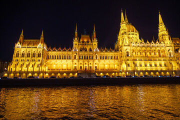 Fototapeta premium Night View of the Hungarian Parliament Building Illuminated at Nighttime along the Danube River in Budapest, Hungary; Beautiful Gothic Revival Architecture and City Lights Reflection