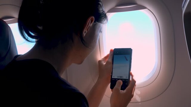 Passenger photographing clouds with mobile phone near airplane window. Holding smartphone camera during flight capturing aerial view. Aviation travel and mobile photography activity