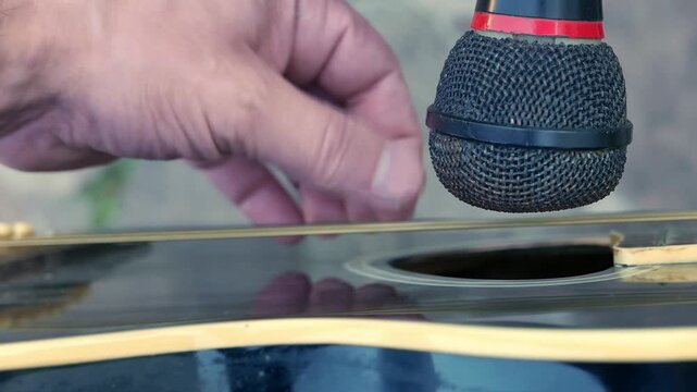 POV (close-up): musician playing acoustic guitar in front of a microphone. A guitar player in front of a microphone. A guitarist strumming a guitar. An artist plucking a guitar. A man playing music