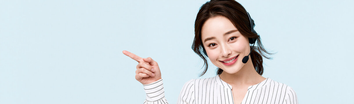 Customer Service Excellence: A friendly Asian female customer service representative with a headset is smiling and pointing to the side, indicating helpfulness and excellent support.