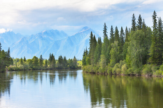 Summer landscape with green forest on banks of Irkut River and silhouettes of Eastern Sayan Mountains in distance on cloudy July day. Natural backdrop. Siberia, Buryatia, Tunka Valley, nature park