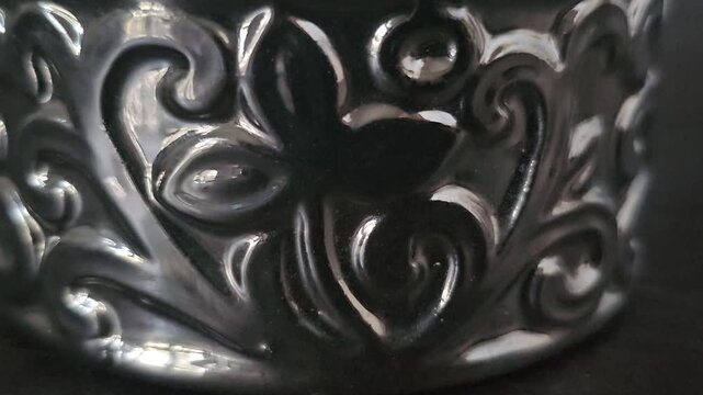 close up of a glass,Dark metallic surface with intricate, swirling floral patterns. Curved design features deep embossed details. Reflective finish highlights decorative craftsmanship