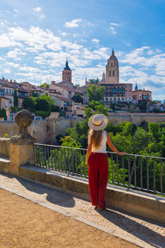 Rear view of young woman tourist in straw hat and red pants looking at cathedral and old town skyline in Segovia, travel destination in Spain