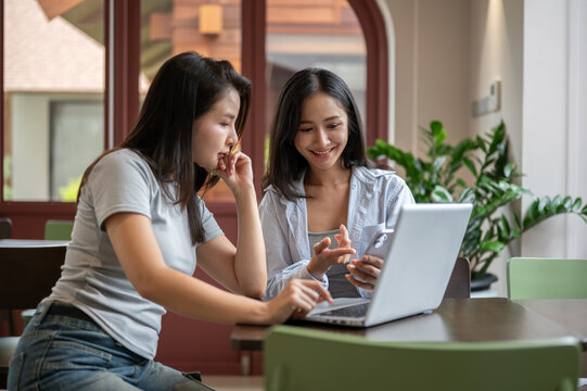 Smiling Asian woman holding smartphone and showing screen to her business partner.