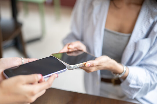 Close up of two Asian women hands tapping smartphones together for data sharing.