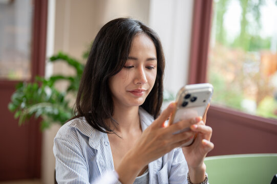 Beautiful Asian woman scrolling on her smartphone screen with a relaxed expression.