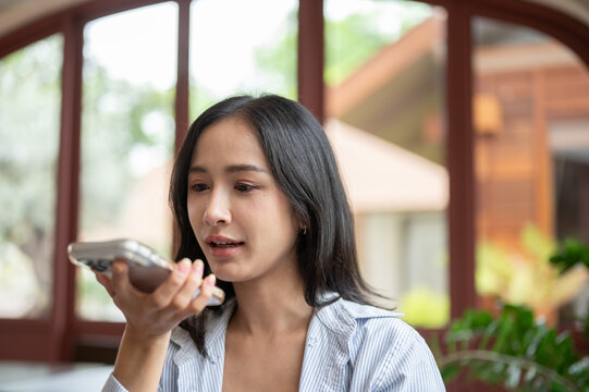 Young Asian woman holding smartphone near mouth to send a voice message.