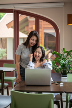 Two cheerful Asian women celebrating achievement with laptop