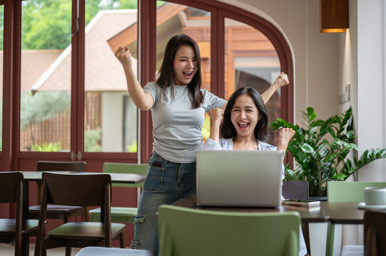 Two young Asian women celebrating online success with laptop