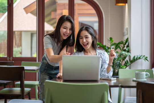 Two happy Asian women pointing at laptop screen during teamwork
