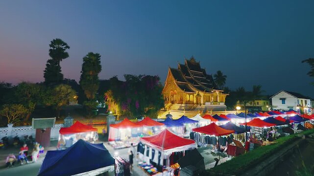 Vibrant night market with illuminated Royal Palace Museum backdrop bustling street stalls and people shopping in evening Luang Prabang Laos