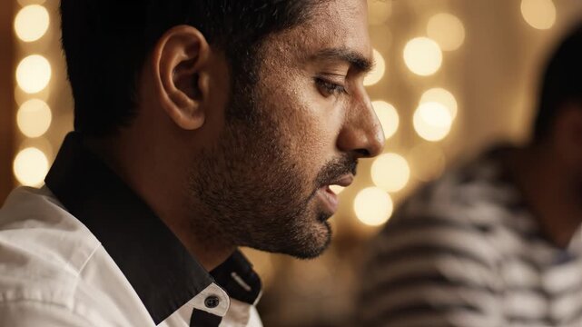 Close-up of Indian man speaking in warm-lit indoor setting with bokeh background