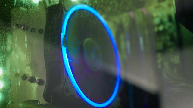 Dust covered cooling fan inside gaming PC with RGB illumination. Closeup through scratched side panel revealing neglected computer hardware and airflow system. PC repair, thermal management, and