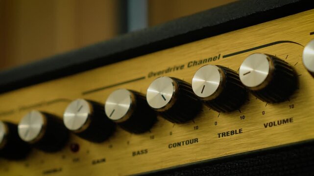 Guitar combo amplifier knobs for gain, bass, contour, and treble control. Shallow depth of field emphasizing analog tone shaping and amplifier settings. Music production, electric guitar equipment