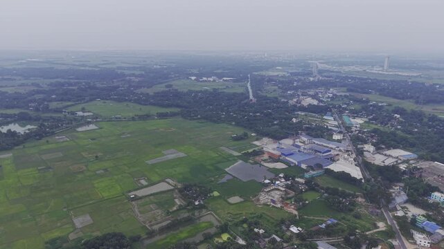A smooth forward drone flight over a semi-urban landscape featuring residential houses, small businesses, open fields, and agricultural farmland, with a distant city skyline visible on the horizon.