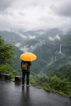 Monsoon traveler with umbrella in misty green mountains
