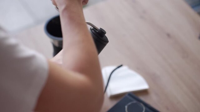 Hands grind coffee with a manual grinder near a pour over dripper on a wooden table. Concept of coffee preparation fresh grinding and manual brewing.
