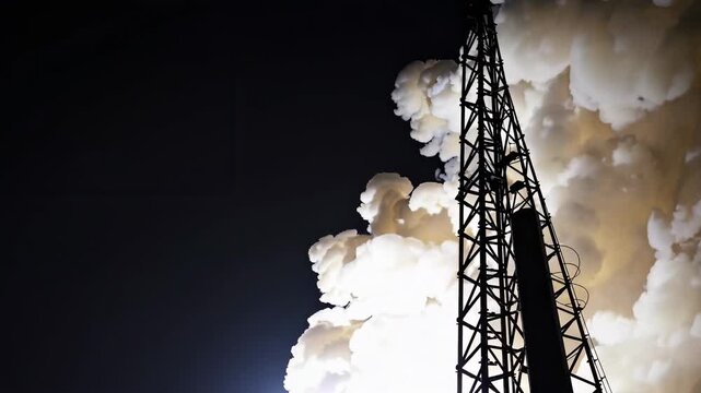 Rocket launch pad with smoke billowing from engines, illuminated by bright light against a dark sky, showcasing the powerful ascent of a spacecraft in motion