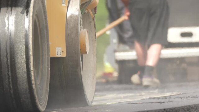The skating rink is being compacted with fresh asphalt. A new layer of asphalt is being laid using a heavy roller. The heavy roller is rolling over the fresh asphalt several times to achieve the