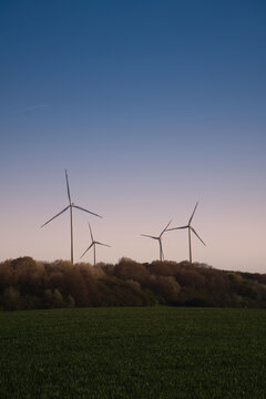Wind turbines as silhouettes on a hill at twilight.