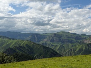 Obraz premium Lush green mountains rise under a cloudy sky, showcasing rolling hills and valleys in a breathtaking natural landscape scene